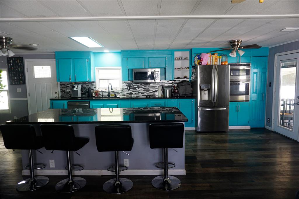 A kitchen features bright blue cabinets, a black granite island with bar stools, and stainless appliances — 143 FLORENCE BOULEVARD, DEBARY, FL