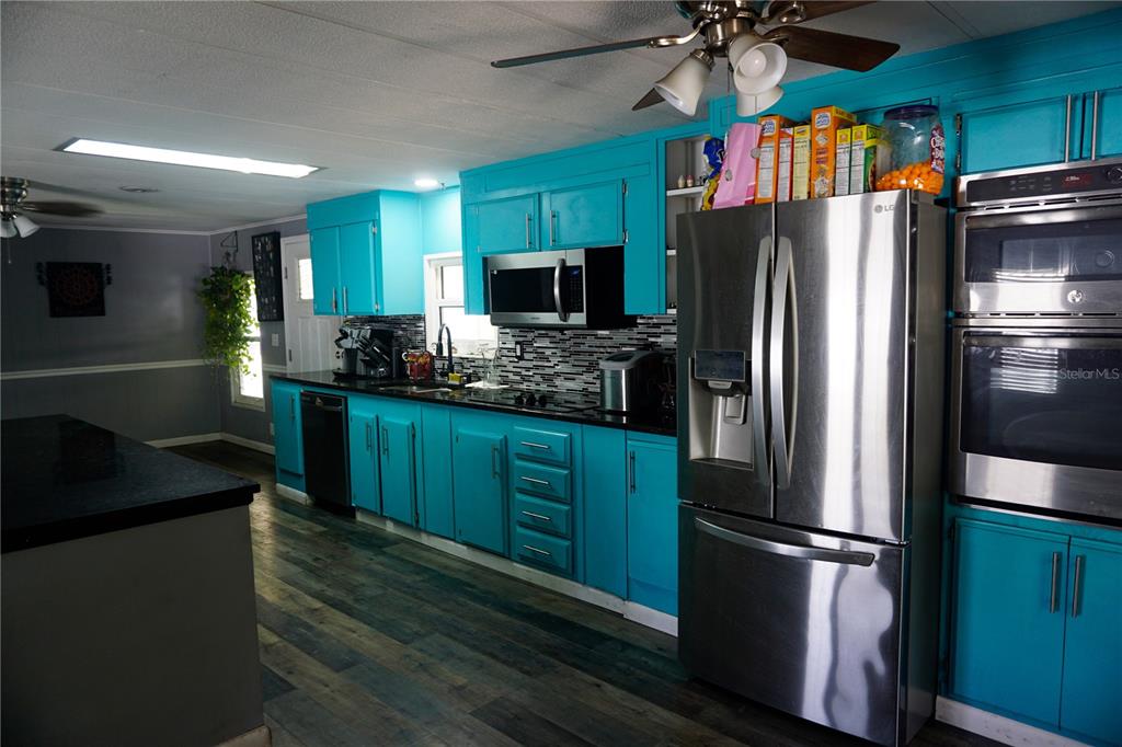 A kitchen features bright turquoise cabinets, stainless steel appliances, and dark countertops — 143 FLORENCE BOULEVARD, DEBARY, FL