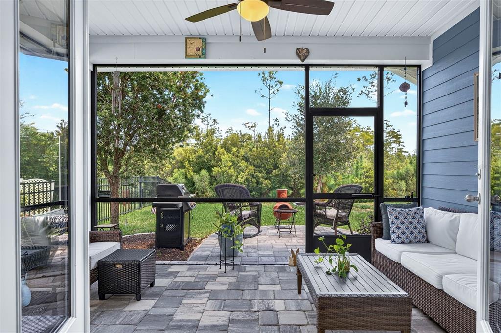A screened-in patio features stone pavers, outdoor furniture, a grill, and a view of trees — 106 NIGHTHAWK LANE, PALM COAST, FL