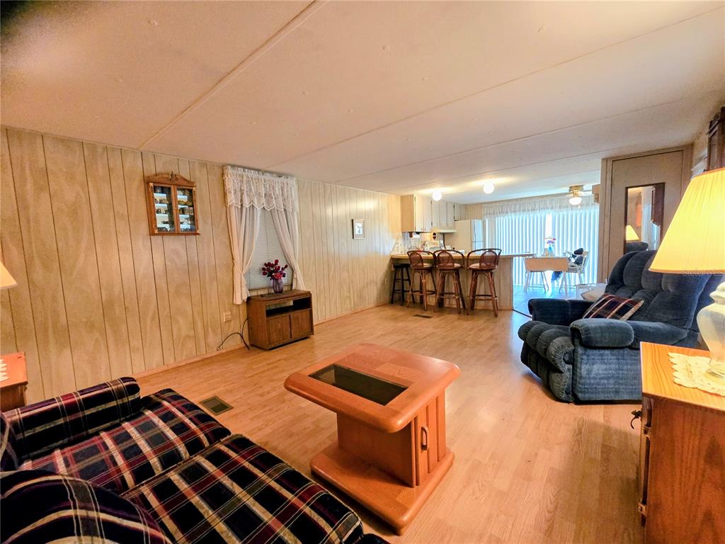 A living room with wood-paneled walls, light wood flooring, and an open kitchen area — 6336 WEALTHY LANE, ZEPHYRHILLS, FL