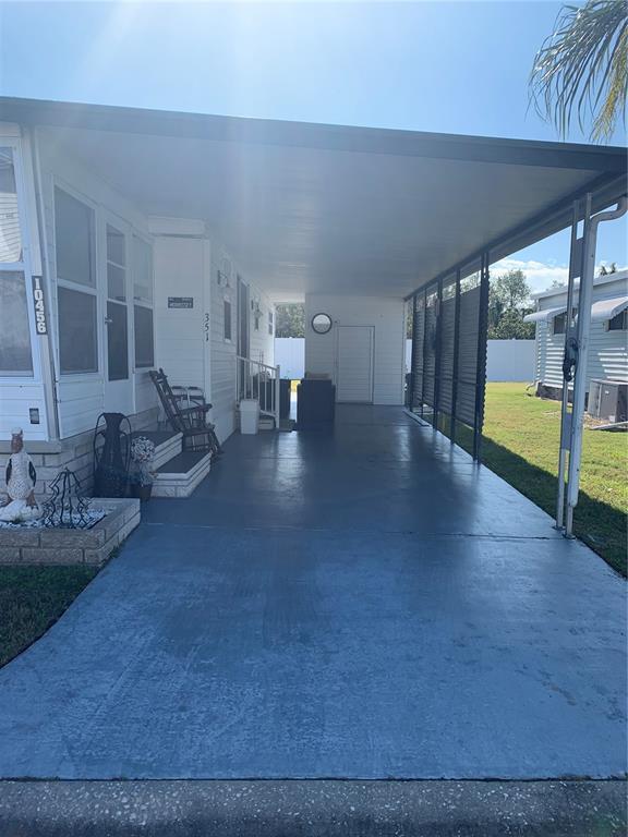 A mobile home exterior features a large covered carport and a concrete driveway — 10456 PEACEFUL DRIVE, LARGO, FL