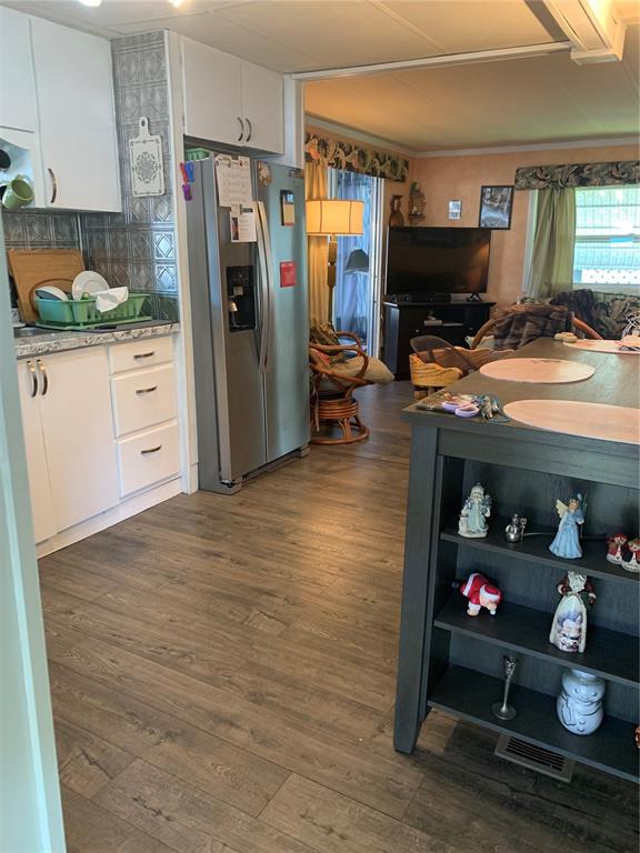 A kitchen with white cabinets and a stainless steel refrigerator opens into a living area — 10456 PEACEFUL DRIVE, LARGO, FL