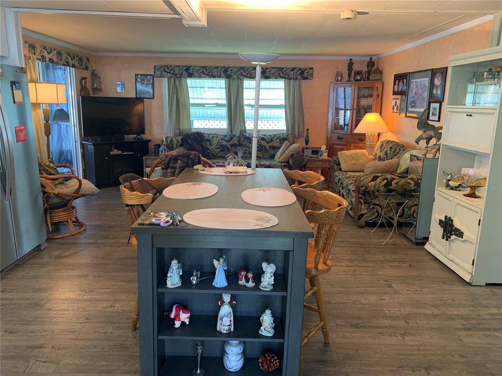 A living room and dining area feature a central island, wood-look flooring, and floral furniture — 10456 PEACEFUL DRIVE, LARGO, FL