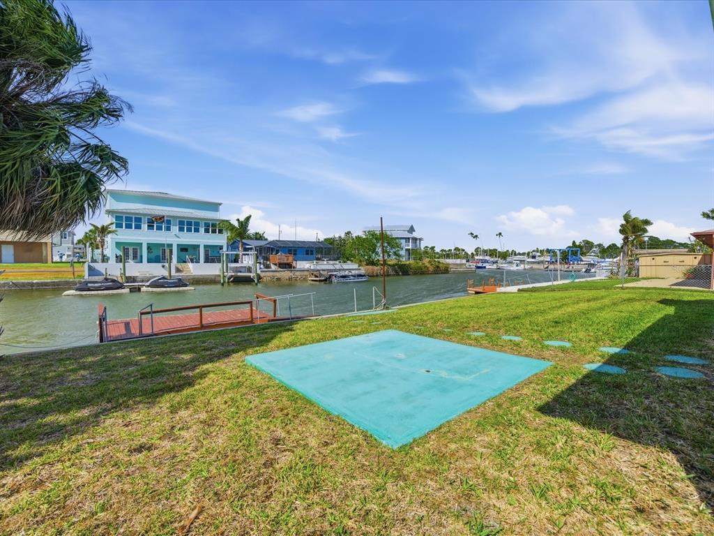 A grassy backyard features a teal concrete pad, a wooden dock, and a canal view — 4069 GULFVIEW DRIVE, HERNANDO BEACH, FL
