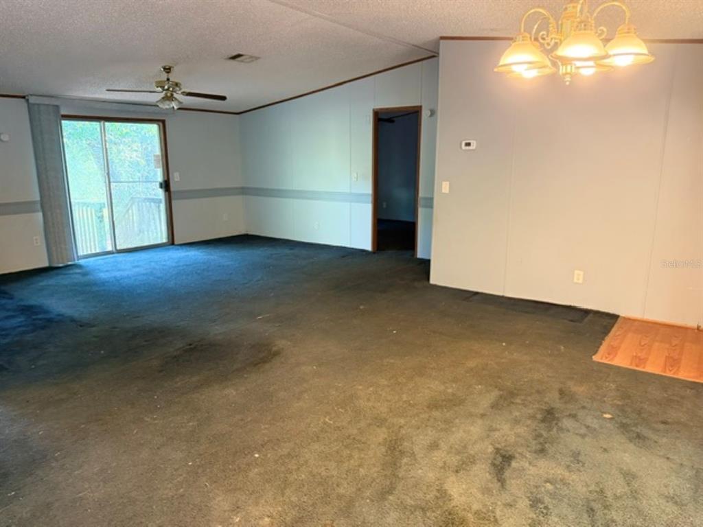 A living room with dark carpeting, a ceiling fan, sliding glass doors, and a chandelier — 18351 SE 62ND PLACE, OCKLAWAHA, FL