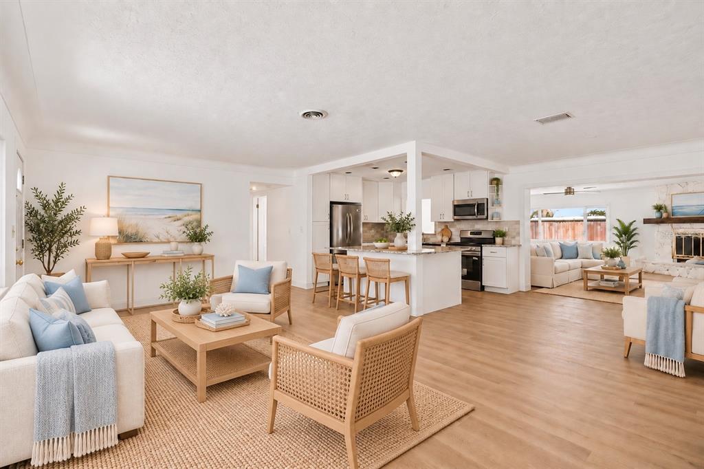 An open-concept kitchen and living area featuring white cabinetry, granite countertops, and wood-look flooring — 7919 CAUSEWAY BOULEVARD S, ST PETERSBURG, FL