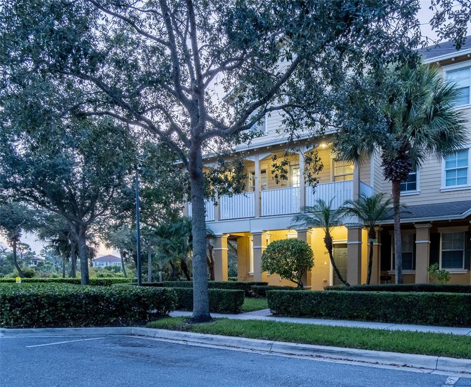 A multi-story tan building with a covered porch and balcony surrounded by manicured hedges — 103 E THATCH PALM CIRCLE, JUPITER, FL