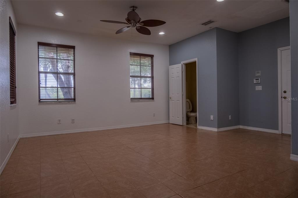 An empty room with tile flooring, two windows with blinds, a ceiling fan, and a bathroom — 103 E THATCH PALM CIRCLE, JUPITER, FL
