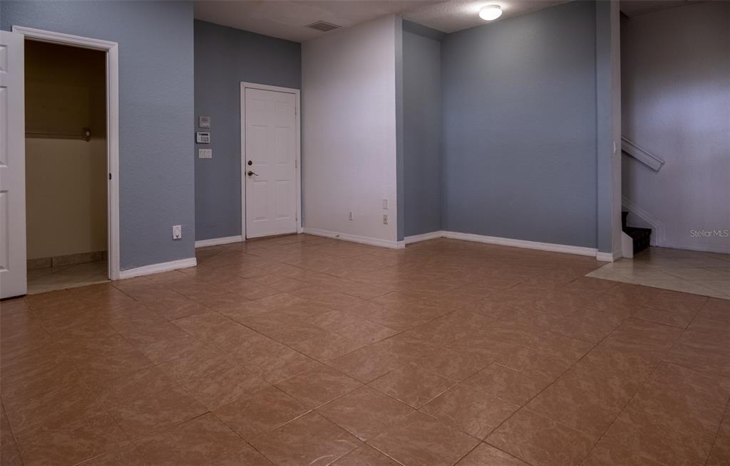 An empty room features light blue walls, large tan floor tiles, and a white door — 103 E THATCH PALM CIRCLE, JUPITER, FL