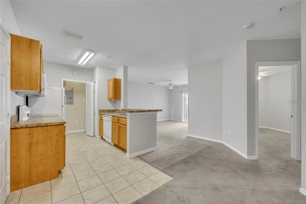 A kitchen with wood cabinets and tile flooring opens into a carpeted living area — 5550 E MICHIGAN STREET UNIT 3216, ORLANDO, FL