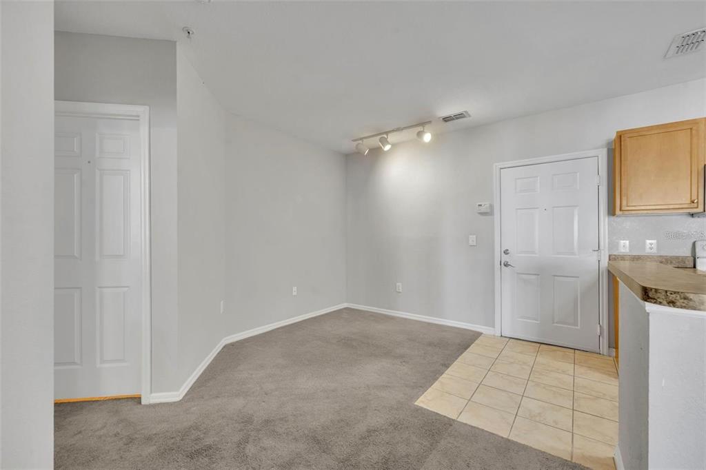 An empty room features gray carpet, a tiled entryway, a white door, and track lighting — 5550 E MICHIGAN STREET UNIT 3216, ORLANDO, FL