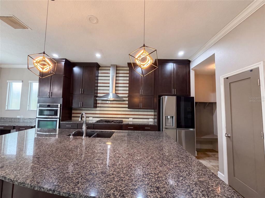 A kitchen features dark wood cabinets, granite countertops, a large island, and stainless steel appliances — 7304 MILESTONE DRIVE, APOLLO BEACH, FL