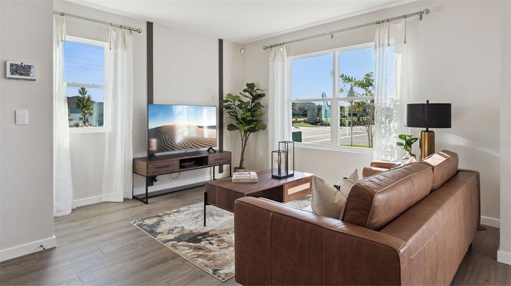 A living room features a brown leather sofa, wood-look flooring, and a television on a stand — 288 PRESTON COVE DRIVE, ST CLOUD, FL