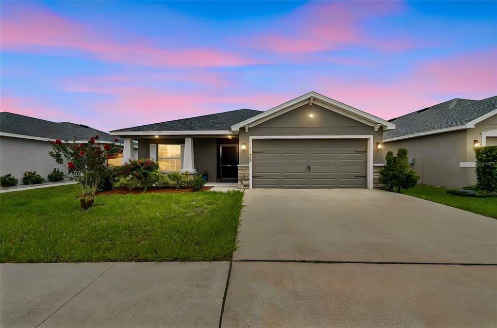 A single-story house with a gray garage, tan siding, and a concrete driveway at sunset — 11669 STONE PINE STREET, RIVERVIEW, FL