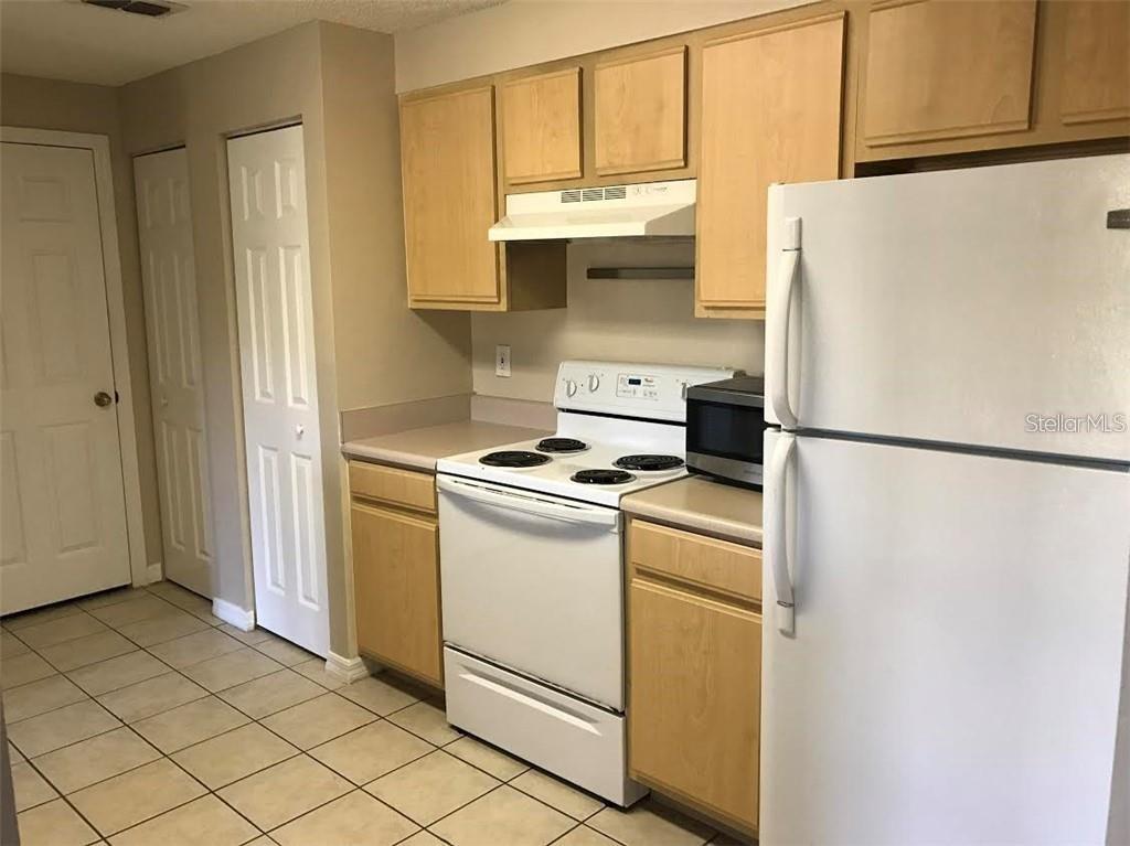 A kitchen with light wood cabinets, white appliances, and beige tile flooring — 10831 WINDSOR WALK DRIVE UNIT 1308, ORLANDO, FL