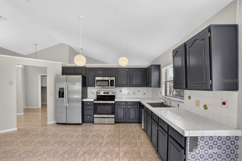 A kitchen with dark gray cabinets, stainless steel appliances, white tile countertops, and tiled floors — 2024 NORFIELD COURT, ORLANDO, FL