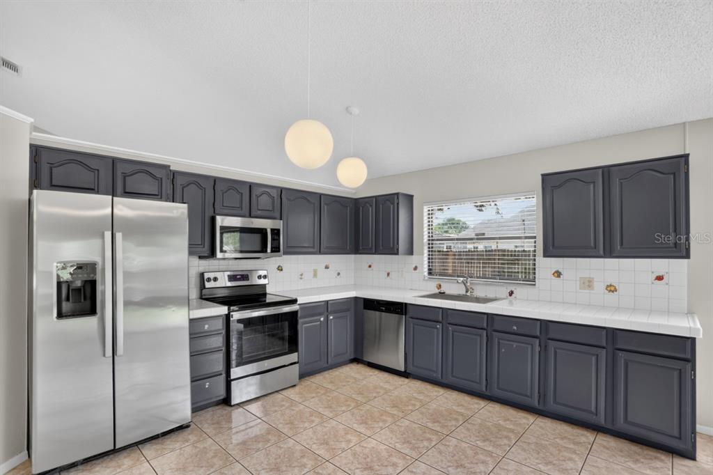 A kitchen features dark gray cabinets, stainless steel appliances, white tile countertops, and tiled flooring — 2024 NORFIELD COURT, ORLANDO, FL