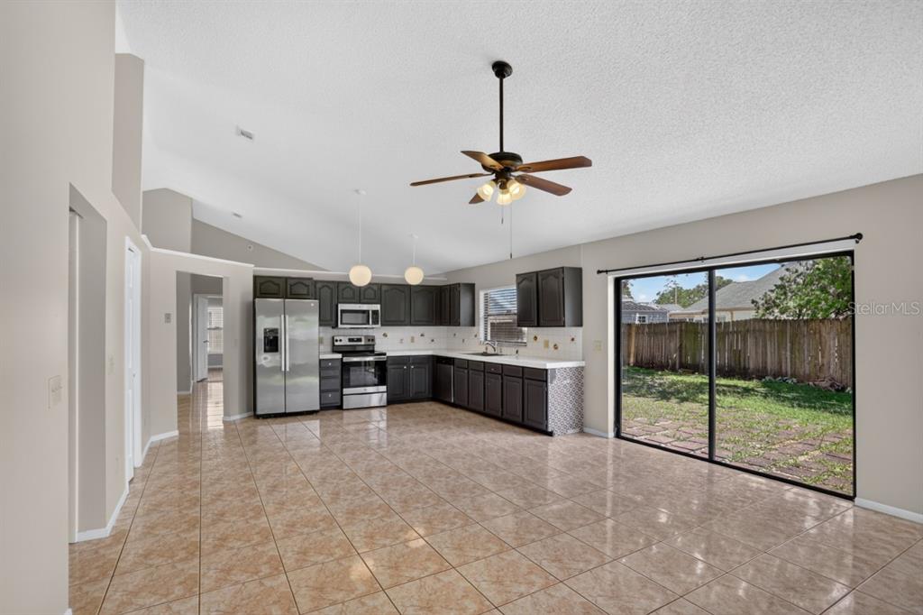 A kitchen with dark cabinets, stainless steel appliances, and tile flooring opens to a backyard — 2024 NORFIELD COURT, ORLANDO, FL