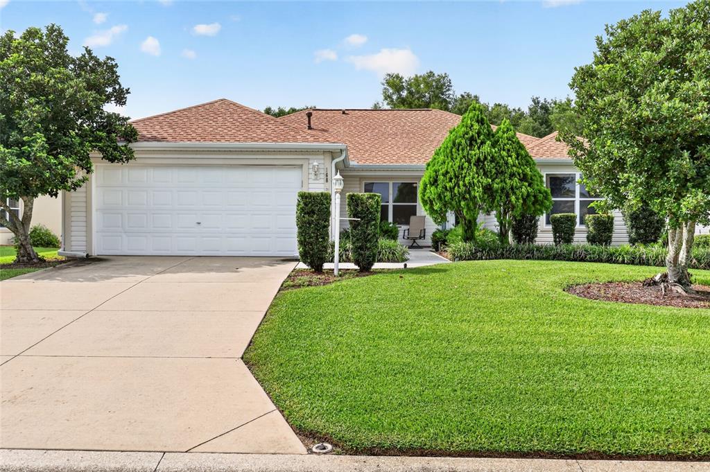 A single-story house with a white garage, tan siding, and a landscaped front lawn — 168 PALERMO PLACE, LADY LAKE, FL