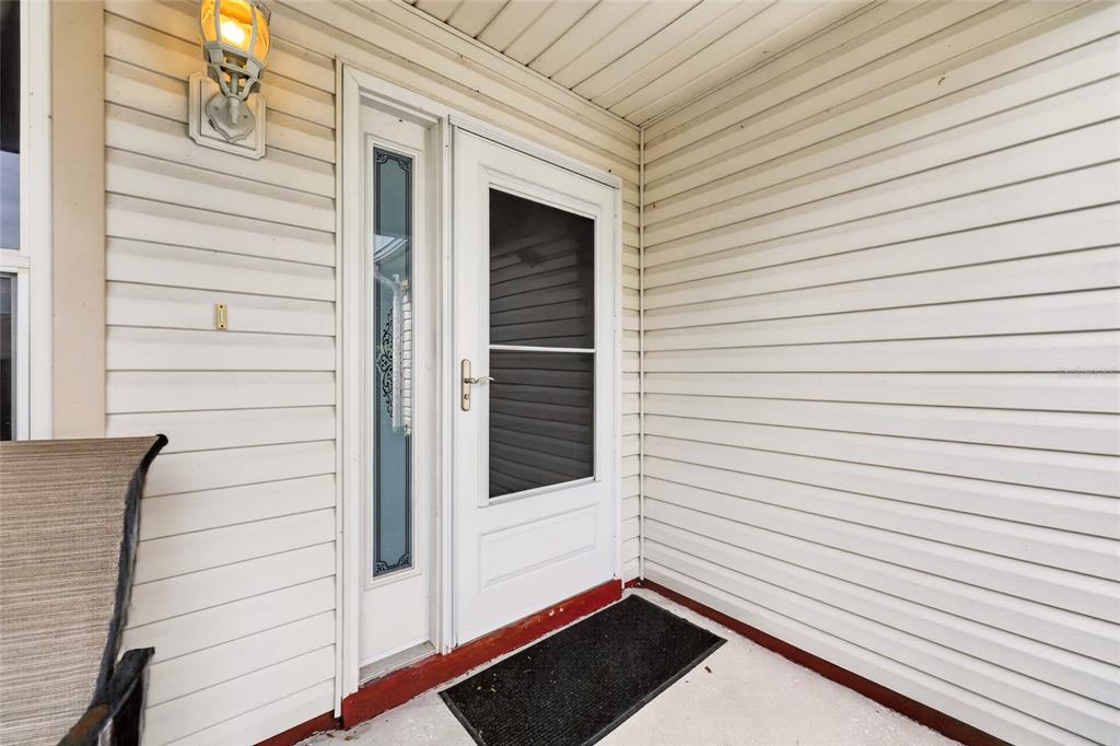 A white front door with a side window and a storm door on a porch — 168 PALERMO PLACE, LADY LAKE, FL