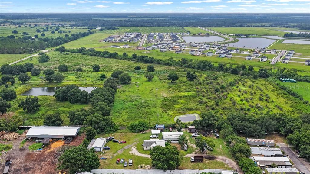 An aerial view shows a rural property with several outbuildings, ponds, and nearby residential development — 5610 CAJUN ROOSTER TRAIL, WIMAUMA, FL