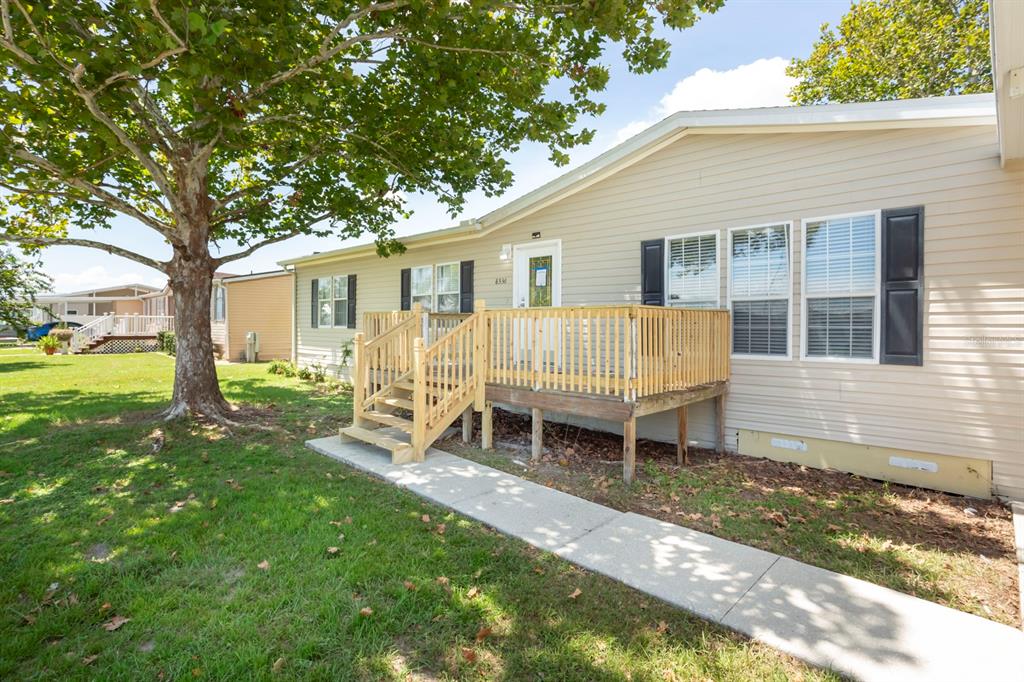 A beige manufactured home features a wooden deck with stairs and a concrete walkway — 8336 CHANCE DRIVE, LAKELAND, FL