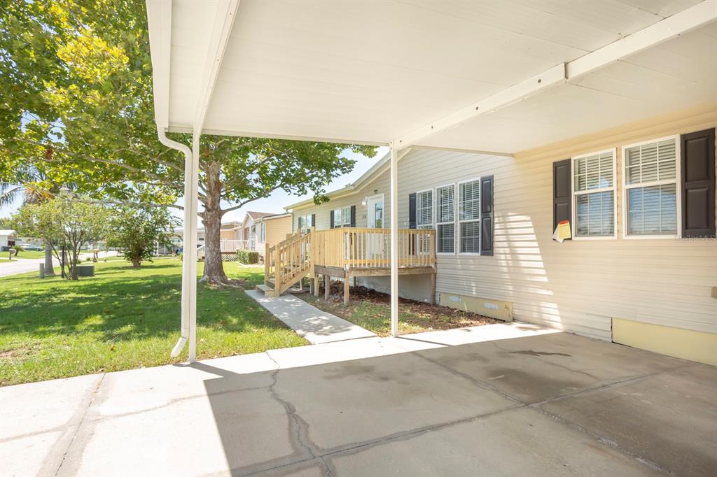 A concrete carport with a white roof cover sits beside a house with a wooden deck — 8336 CHANCE DRIVE, LAKELAND, FL