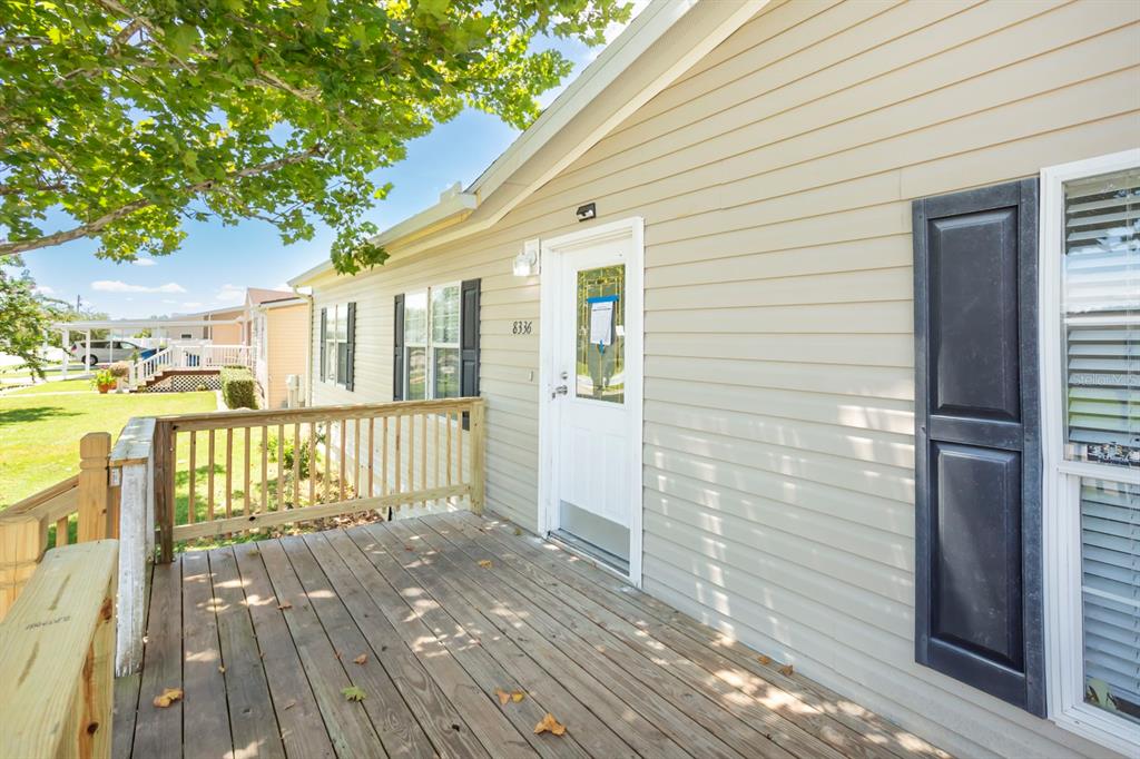 A wooden deck leads to the front entrance of a house with light-colored vinyl siding — 8336 CHANCE DRIVE, LAKELAND, FL