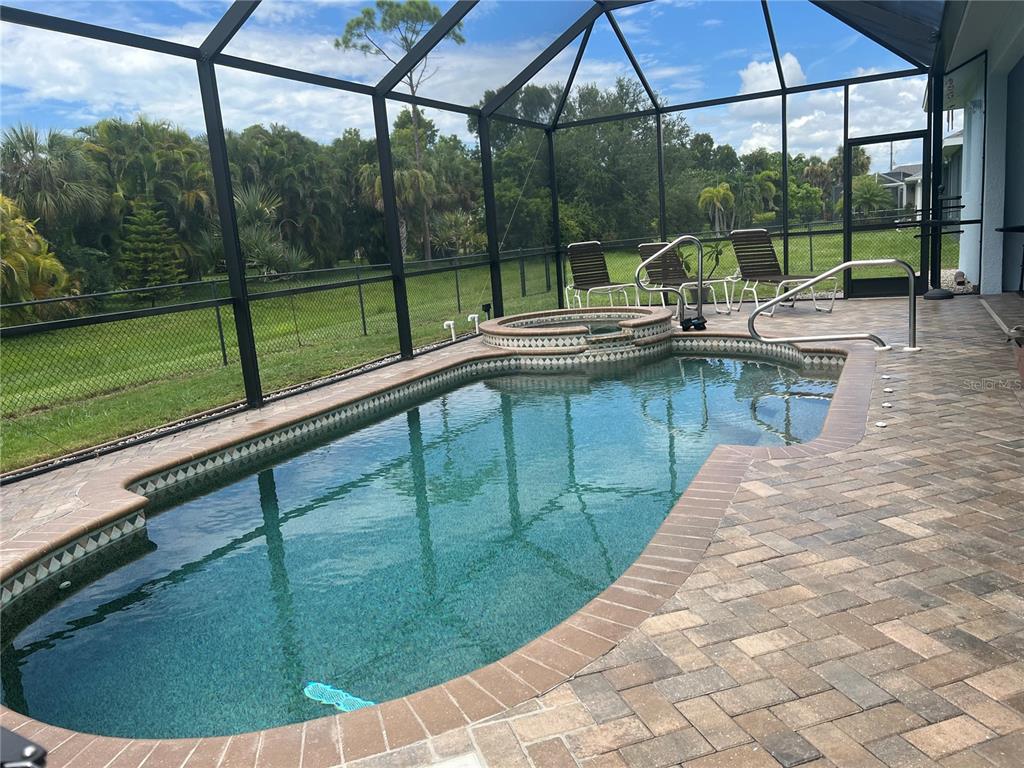 A screened-in swimming pool and spa with brick pavers and lounge chairs in a backyard — 11 BROADMOOR LANE, ROTONDA WEST, FL
