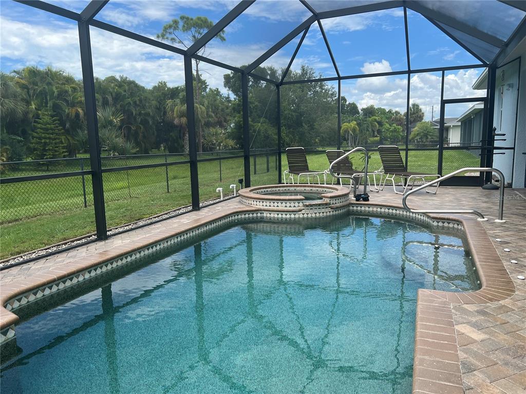 A screened-in swimming pool and raised hot tub sit on a brick paver patio — 11 BROADMOOR LANE, ROTONDA WEST, FL
