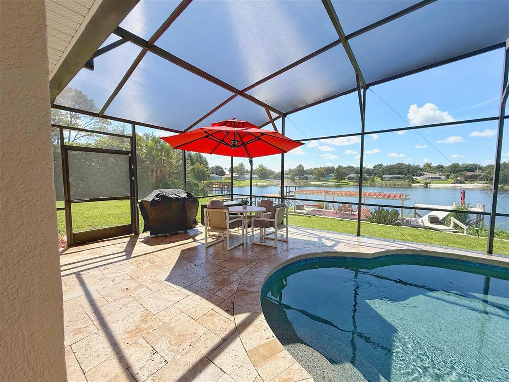 A screened-in pool patio features stone pavers, a dining set, and a view of a lake — 11416 LAKE KATHERINE CIRCLE, CLERMONT, FL