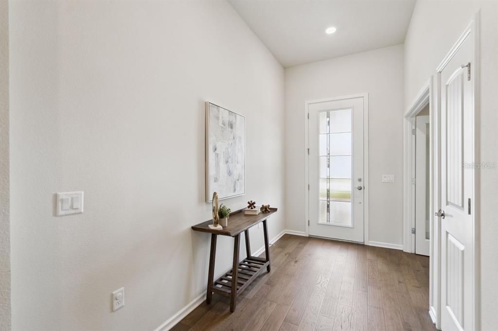 An entryway features hardwood floors, a wooden console table, wall art, and a glass-paneled front door — 15084 CANOPY COVER DRIVE, WINTER GARDEN, FL