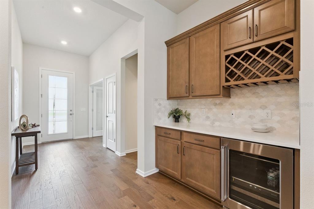 A hallway features a built-in wet bar with wood cabinets, wine storage, and stainless appliance — 15084 CANOPY COVER DRIVE, WINTER GARDEN, FL