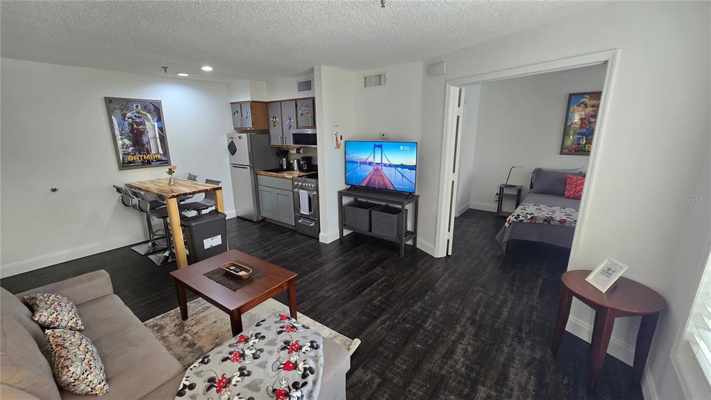 A living room and kitchen area with dark wood flooring, a sofa, and a bedroom — 3100 PARKWAY BOULEVARD UNIT 123, KISSIMMEE, FL