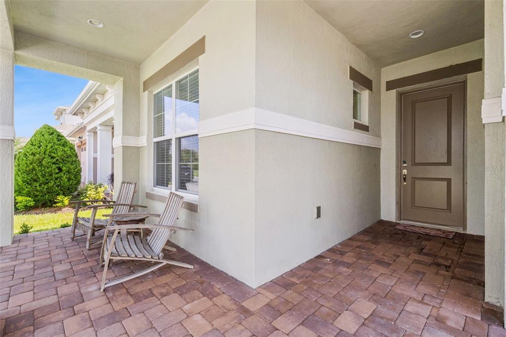 A covered front porch features a brick paver floor, two wooden chairs, and a brown door — 5087 TWIN LAKES BOULEVARD, ST CLOUD, FL