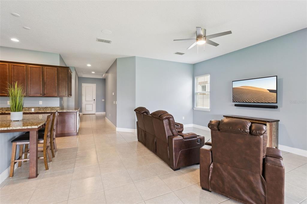 A living room with brown leather furniture, a wall-mounted television, and an adjacent kitchen area — 5087 TWIN LAKES BOULEVARD, ST CLOUD, FL