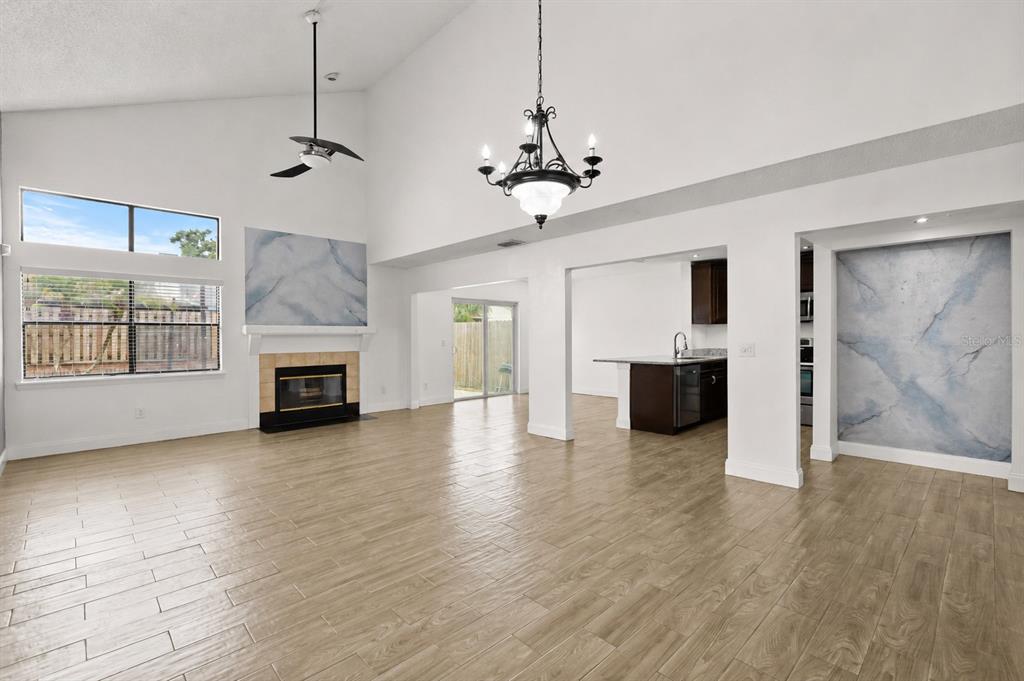 A living room with a fireplace, vaulted ceiling, chandelier, and carpeted stairs leading upward — 3109 BRIDGEFORD DRIVE, ORLANDO, FL