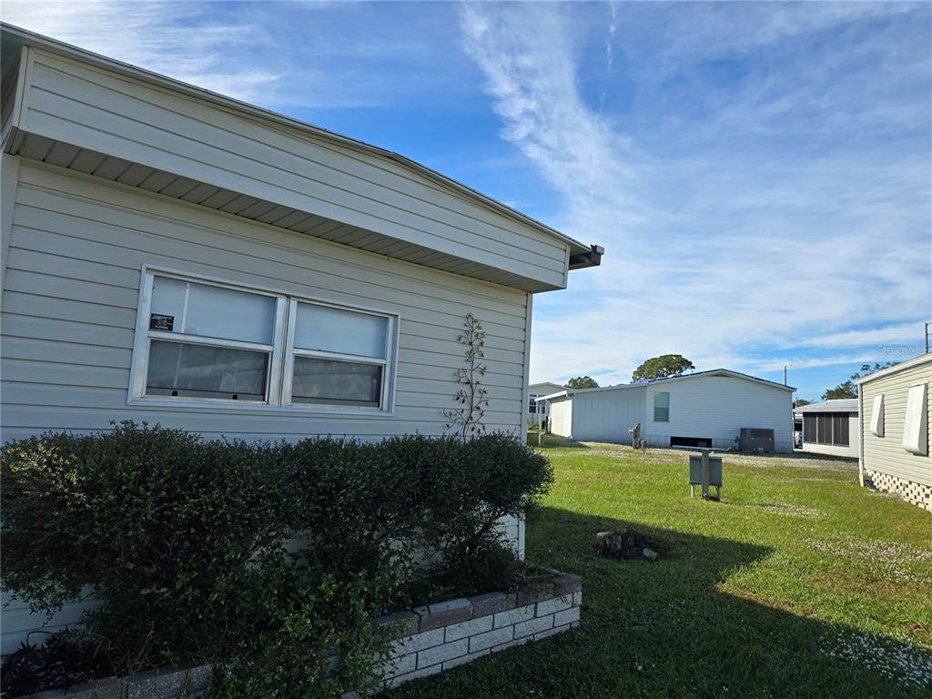 A view of a light-colored mobile home exterior with a small garden bed and lawn — 5316 53RD AVENUE E UNIT F21, BRADENTON, FL