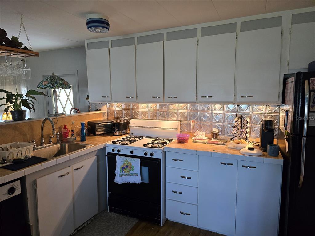 A kitchen features white cabinets, a tiled backsplash, a gas stove, and a stainless sink — 5316 53RD AVENUE E UNIT F21, BRADENTON, FL