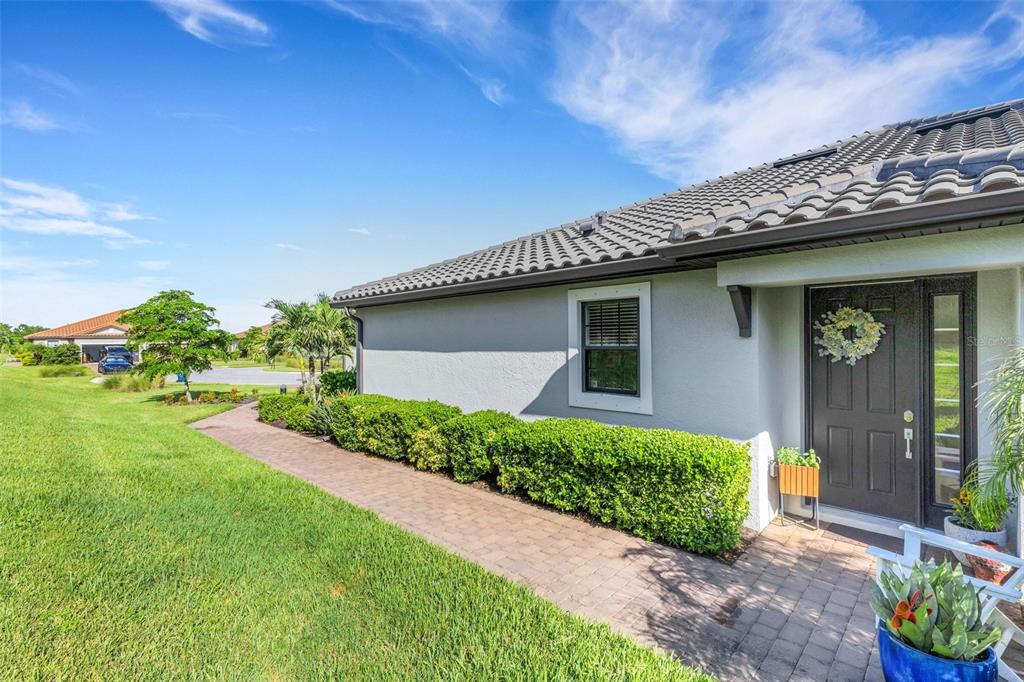 A paved walkway leads to the front entrance of a house with gray stucco walls — 4773 TORTONA COURT, BRADENTON, FL