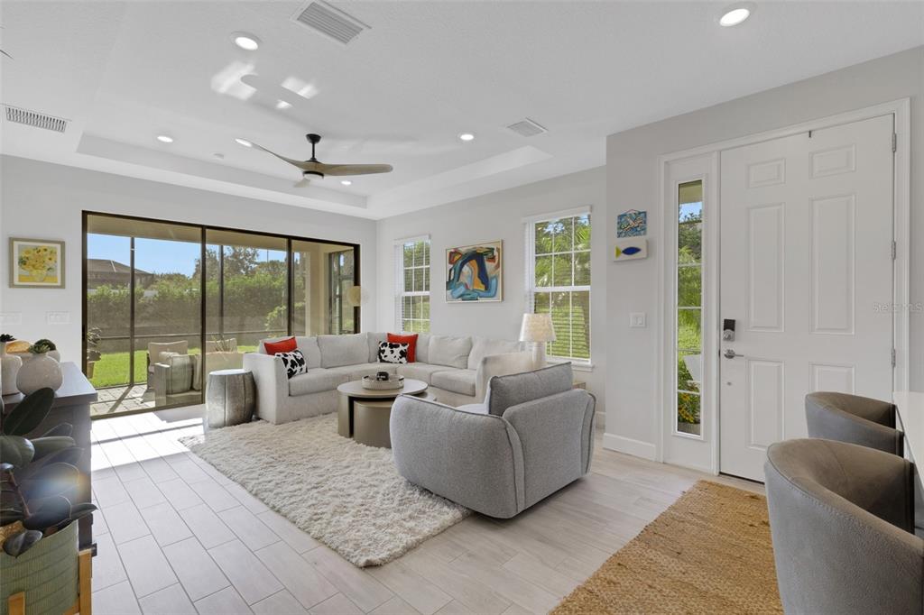A bright living room features a sectional sofa, gray armchair, and sliding glass doors — 4773 TORTONA COURT, BRADENTON, FL