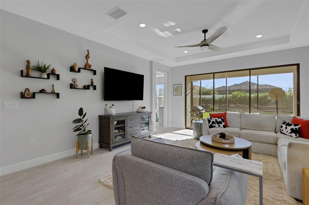 A living room features a gray sectional, a wall-mounted television, and sliding glass doors — 4773 TORTONA COURT, BRADENTON, FL