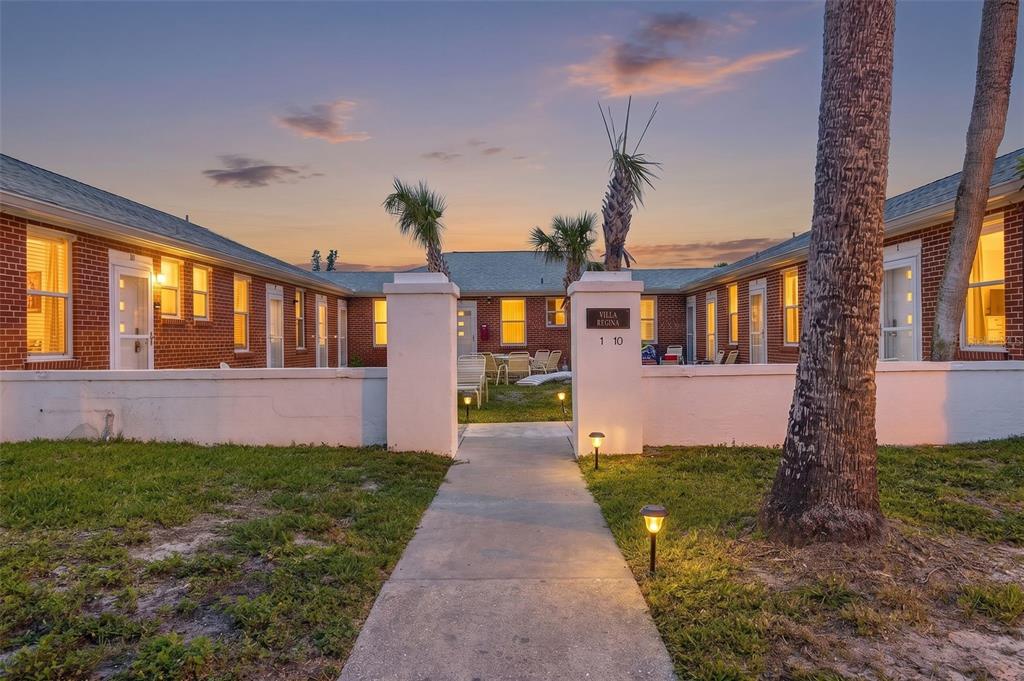 A brick U-shaped apartment complex with a central courtyard and a concrete walkway at dusk — 908 VILLAS DRIVE UNIT 10, VENICE, FL