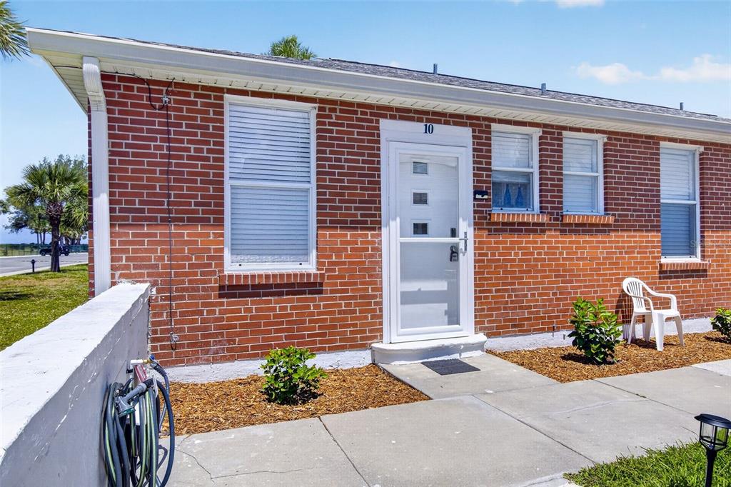 A red brick exterior of a single-story building features a white door and windows — 908 VILLAS DRIVE UNIT 10, VENICE, FL