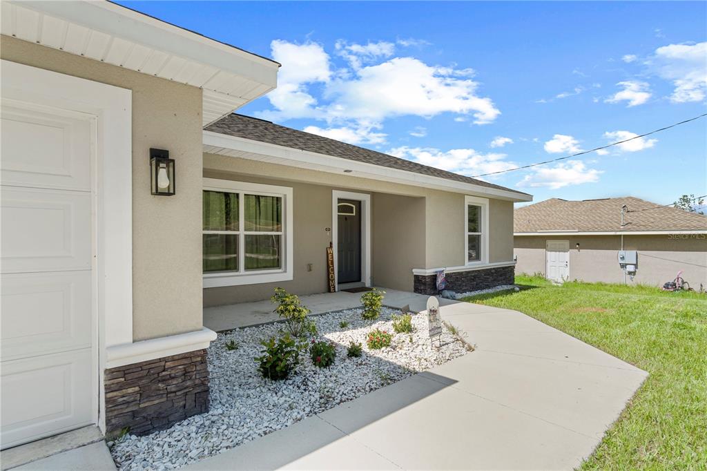 The exterior of a single-story house features a concrete walkway, stone accents, and landscaping — 18 DOGWOOD TRAIL COURSE, OCALA, FL