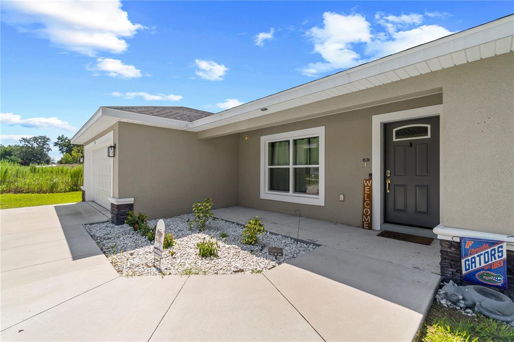 A tan house exterior features a concrete driveway, a small rock garden, and a front door — 18 DOGWOOD TRAIL COURSE, OCALA, FL