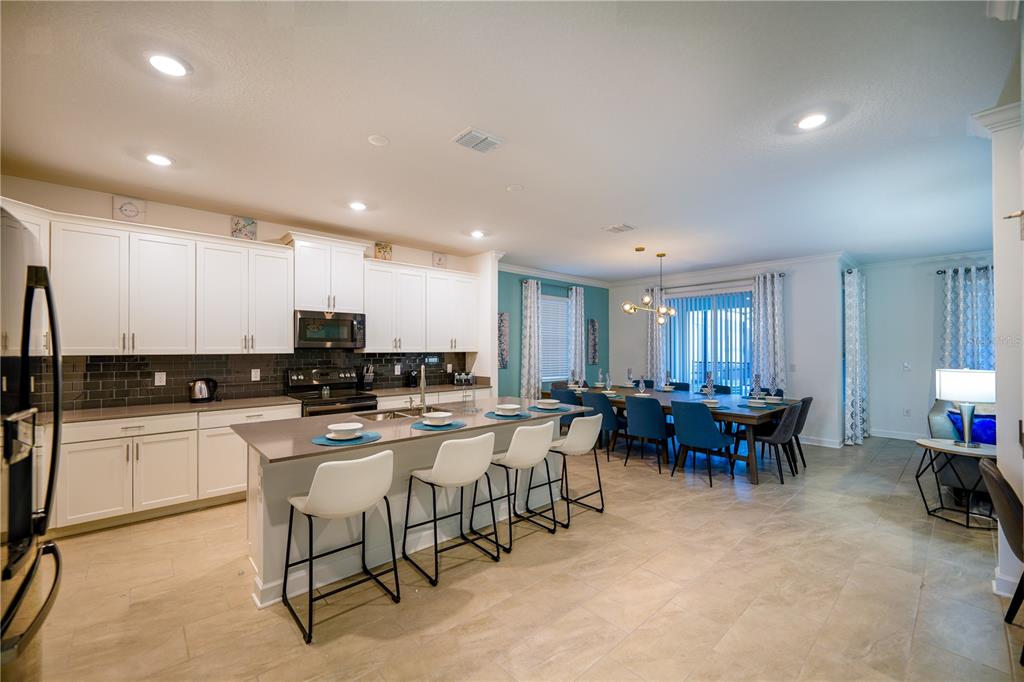 A kitchen with white cabinets and a large island opens to a dining area — 3020 PROTAGONIST STREET, KISSIMMEE, FL