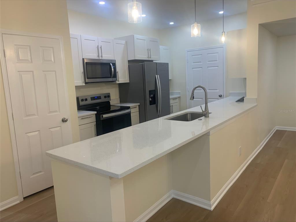 A kitchen features white cabinets, stainless steel appliances, a quartz countertop, and a breakfast bar — 280 CELEBRATION BOULEVARD UNIT 27104, CELEBRATION, FL