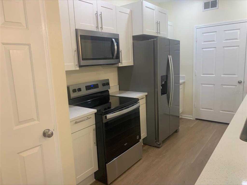 A kitchen features white cabinets, stainless steel appliances, and light wood-look flooring — 280 CELEBRATION BOULEVARD UNIT 27104, CELEBRATION, FL