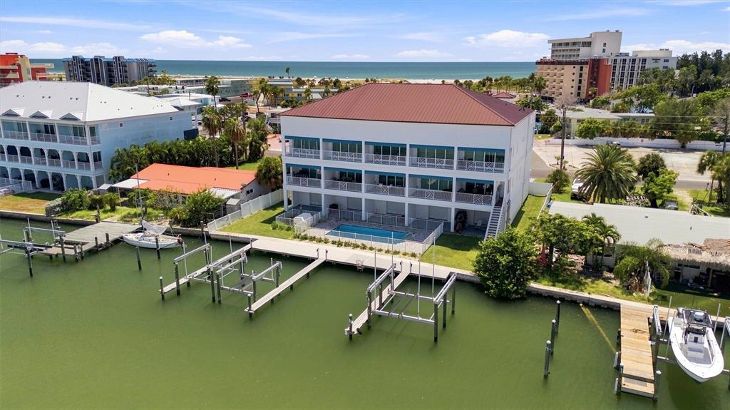 An aerial view shows a multi-story building with a pool and boat docks on a canal — 11797 1ST STREET E, TREASURE ISLAND, FL